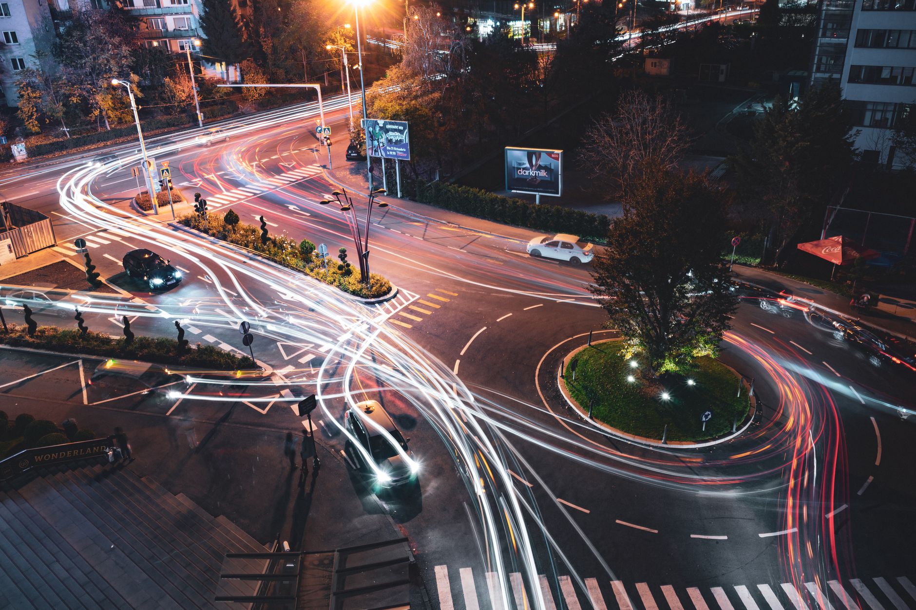 A busy city junction at night seen from above, traffic threading through it from every lane at once