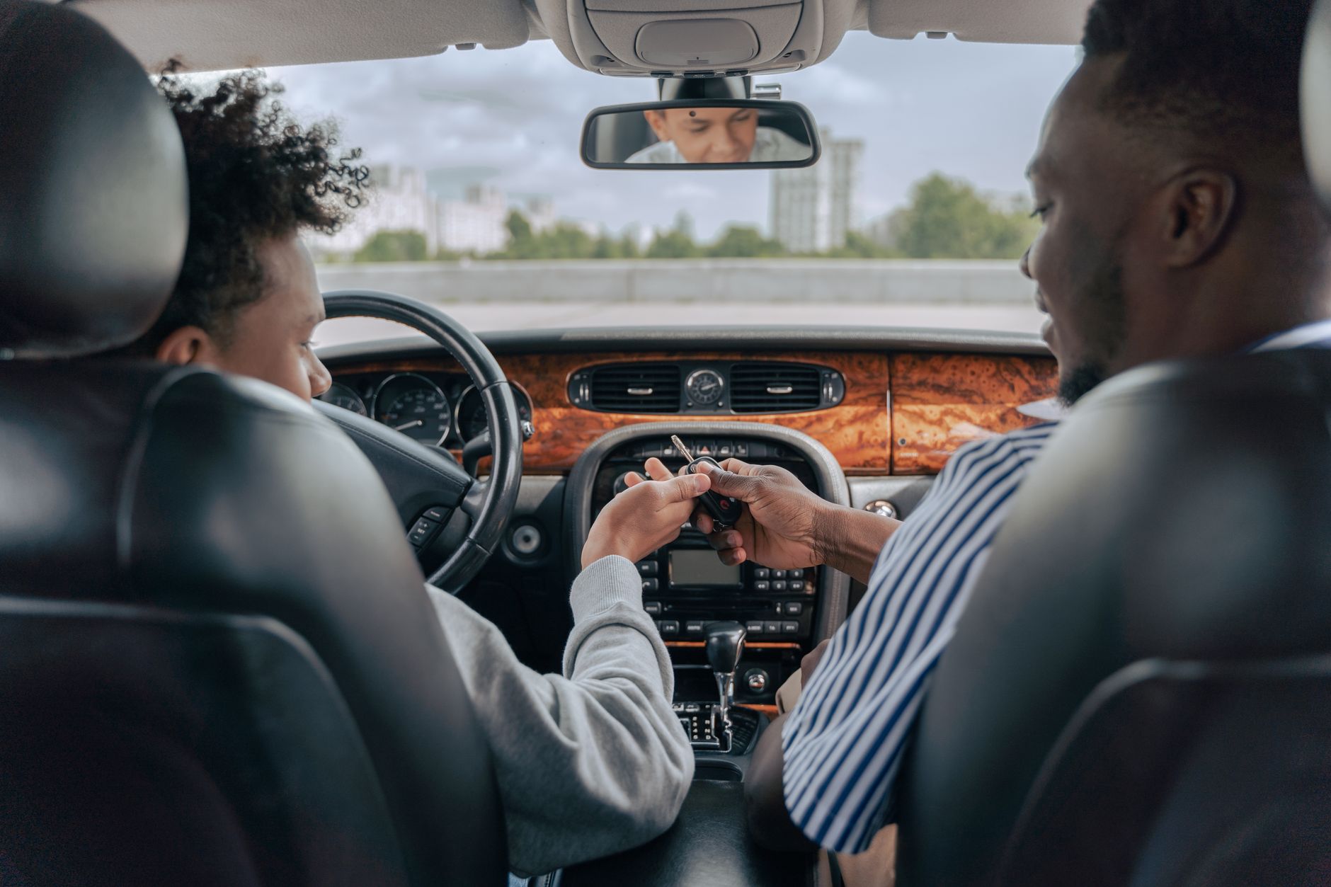 A learner and an instructor sitting in a car mid-lesson, the learner's hands on the wheel and the instructor watching the road