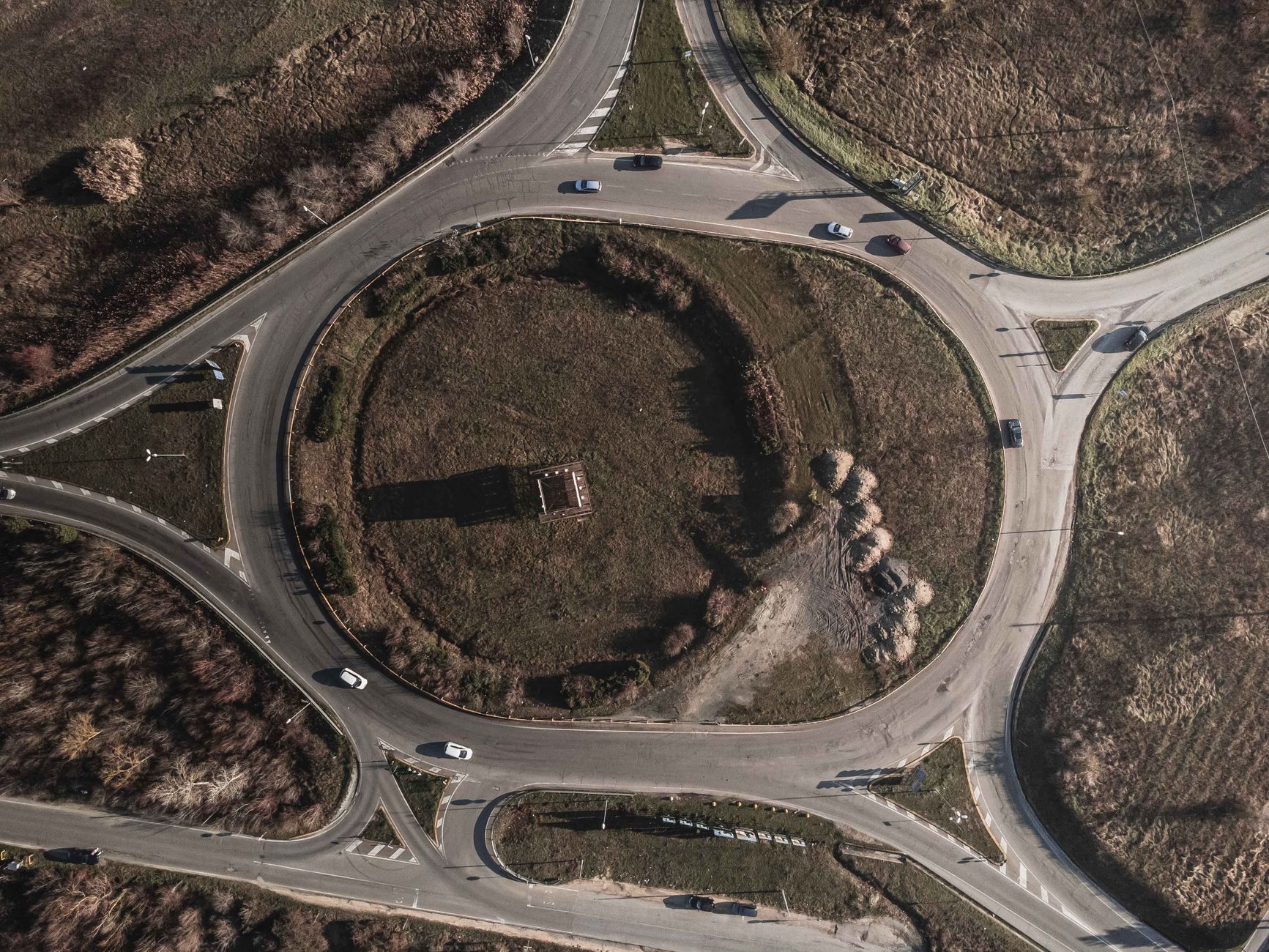 An aerial view of a road roundabout, showing the circular flow and the lanes feeding into it